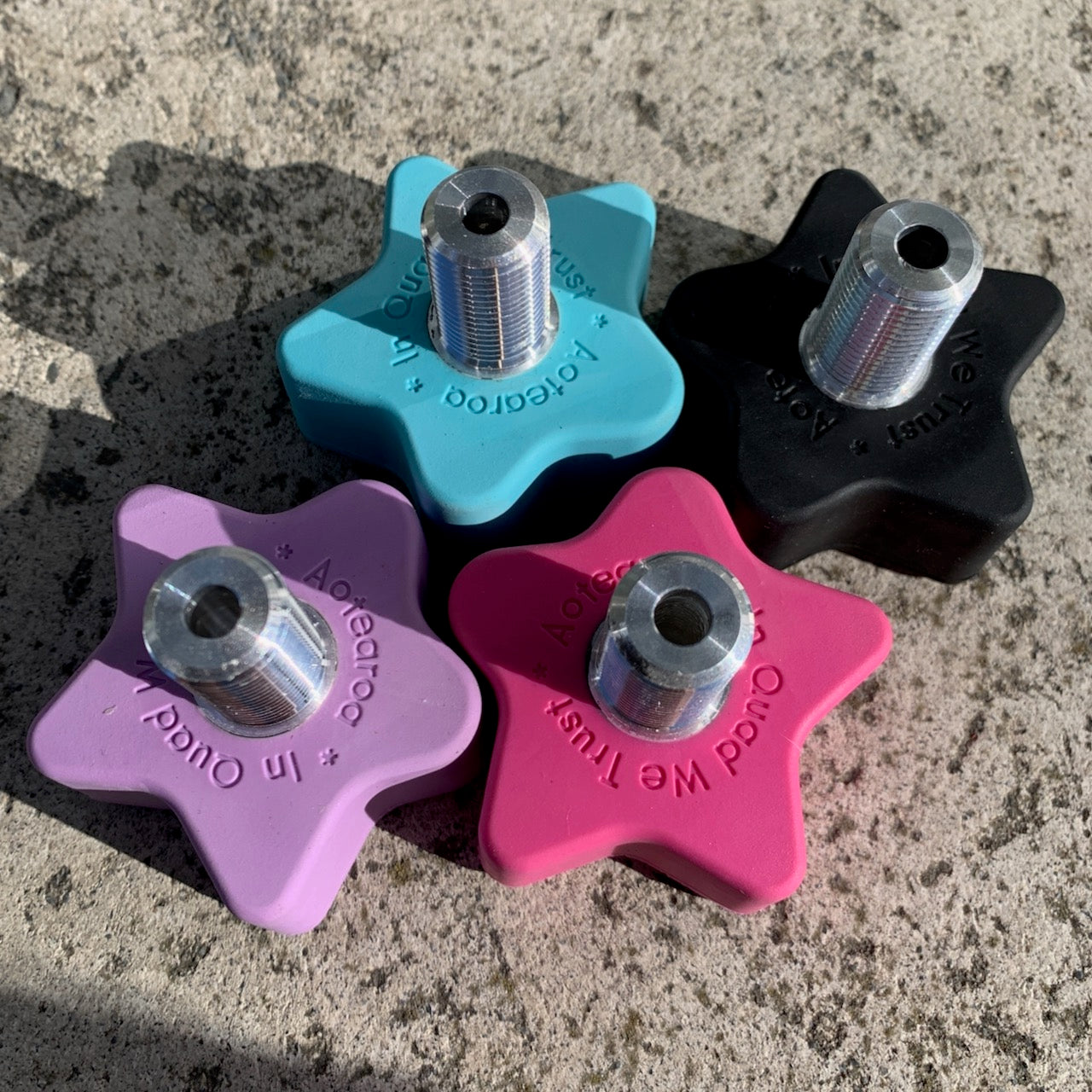 A set of four roller skate toe stops in different colors: blue, pink, black, and purple. Each toe stop has a star shape with a metallic stem on top.